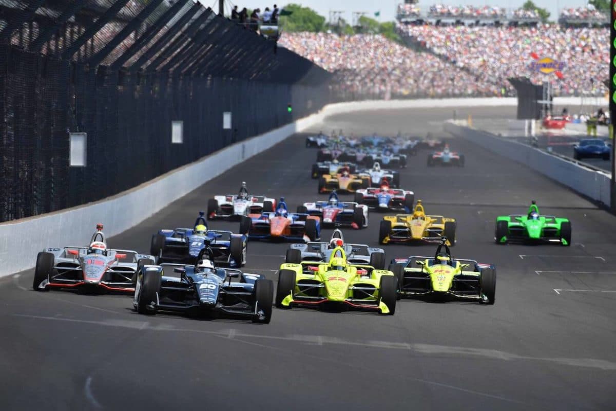 Indy 500 cars racing around track with crowd in background