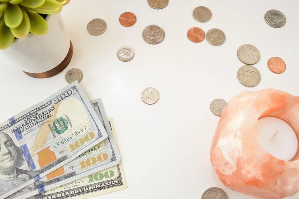 one hundred dollar bills on table with change, a plant and pink candle