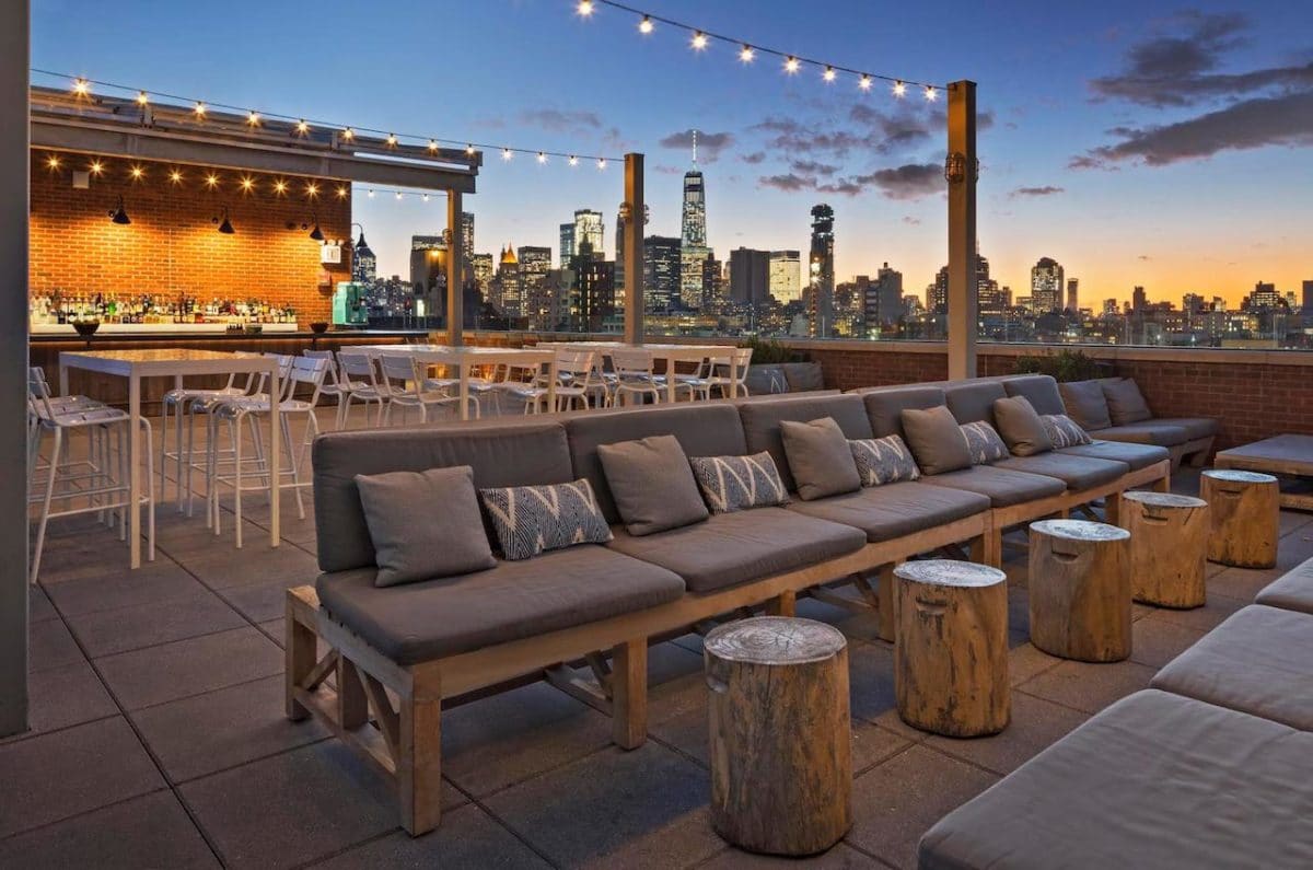 rooftop bar overlooking manhattan with lights strung and bar in background