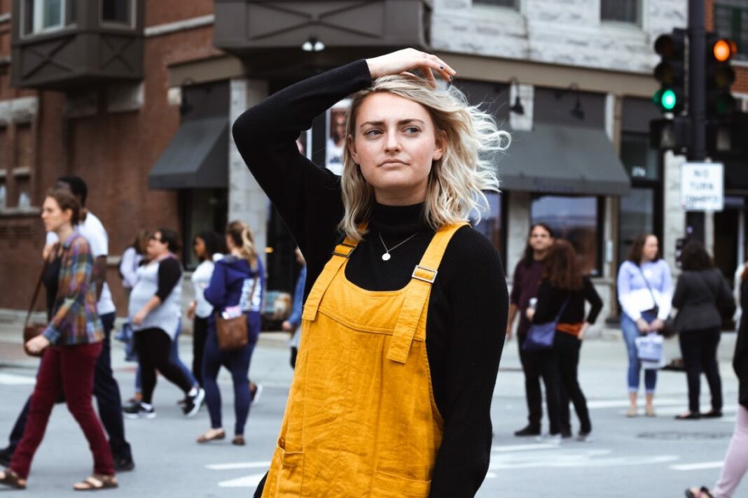 woman in yellow overalls walking in street with hand on head