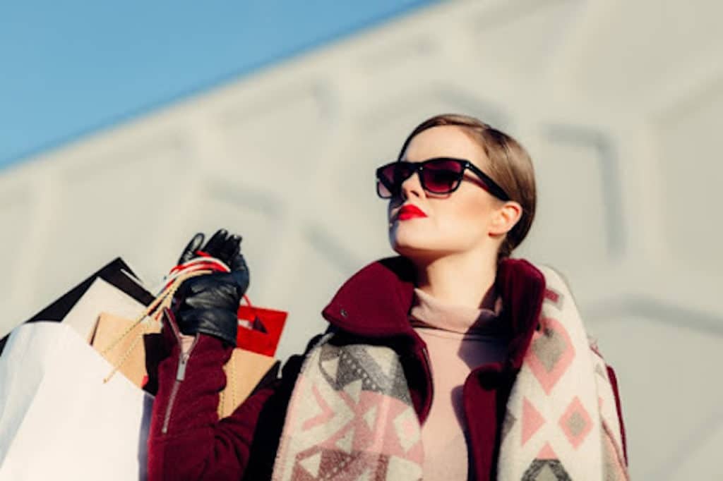 woman outside looking up to the sky in sunglasses and carrying shopping bags